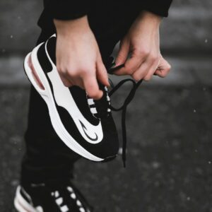 Close-up of an athlete tying black and white sneakers on a street, highlighting fitness and outdoor exercise.
